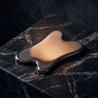 Stainless steel gua sha on a dark marble vanity