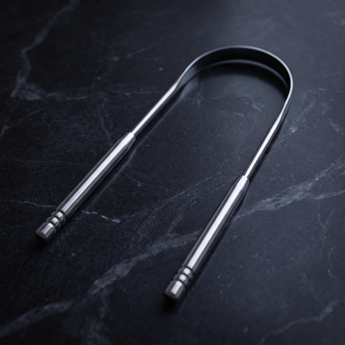 Stainless steel tongue scraper on dark marble