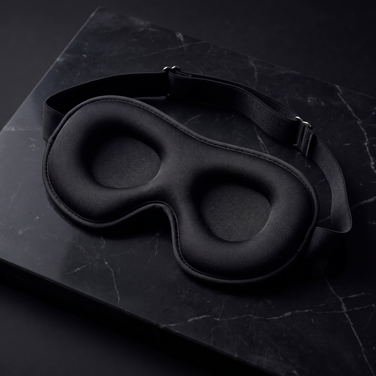 Black 3D contoured sleep mask on dark marble