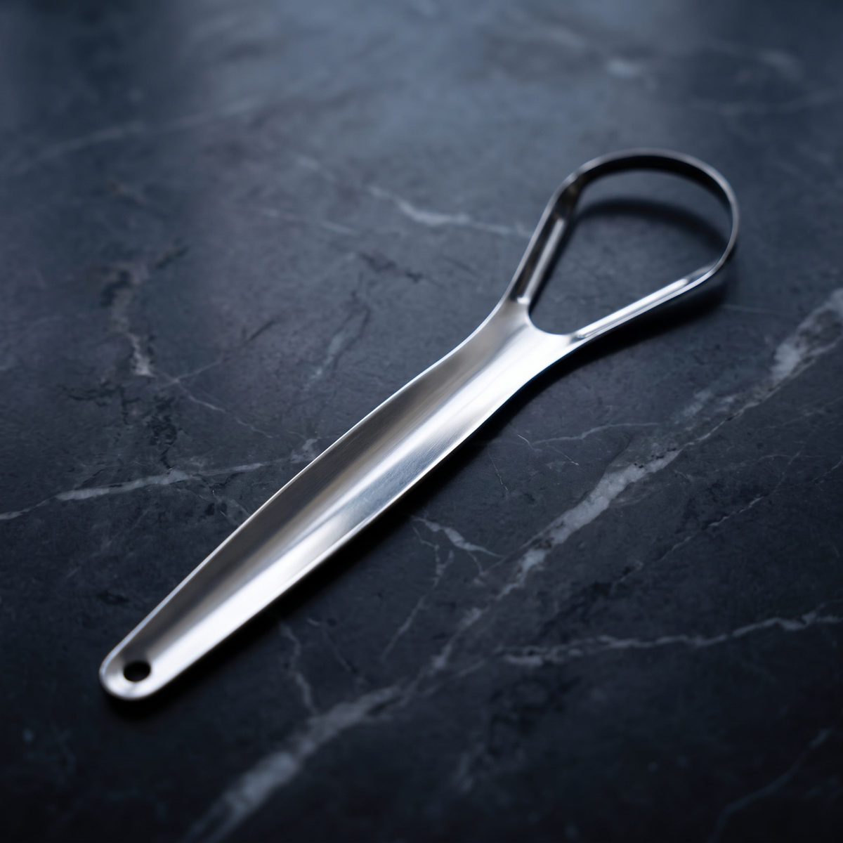 Silver stainless steel tongue scraper on dark marble